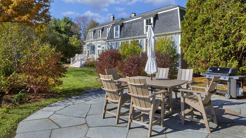 Outdoor seating/dining area on a sunny day, surrounded by lush greenery on flagstone