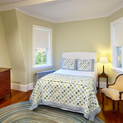 Bedroom with 1 full sized bed and dresser, side chair, flanked by two windows