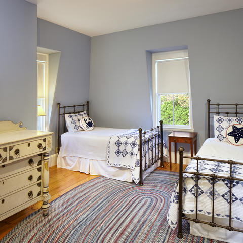 Bedroom with two twin beds and a dresser, hard flooring with a rug, and two windows in view