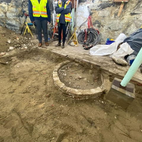 The buried well is covered by layers of dirt and just surfacing through the earth with construction team members standing by